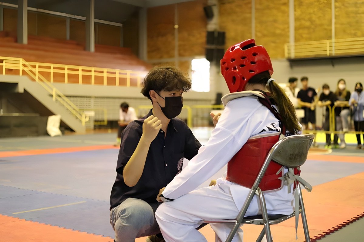 Coach speaking with a young Taekwondo athlete in red gear between rounds